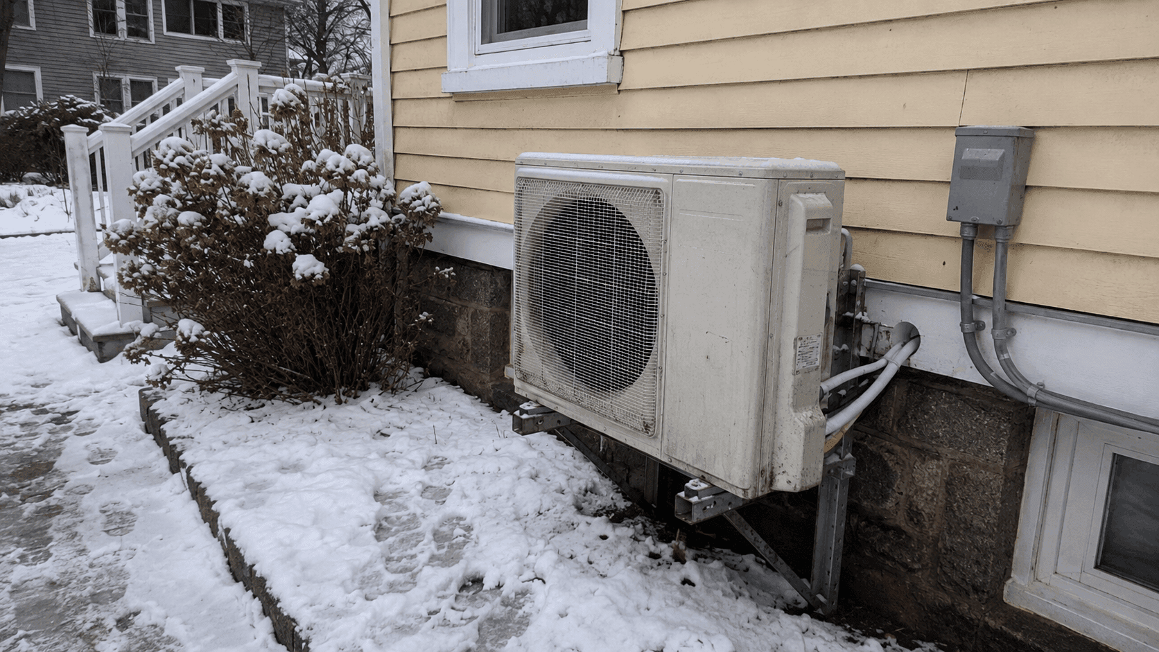 Cold-climate heat pump running outside a snow-covered Greater Boston home during winter heating season