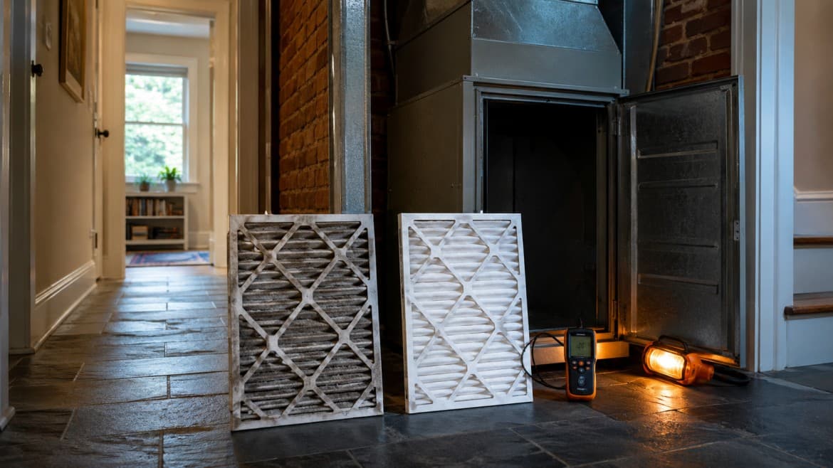 Homeowner holding a loaded one-inch HVAC filter up to a light to check whether it needs replacing in a Greater Boston home